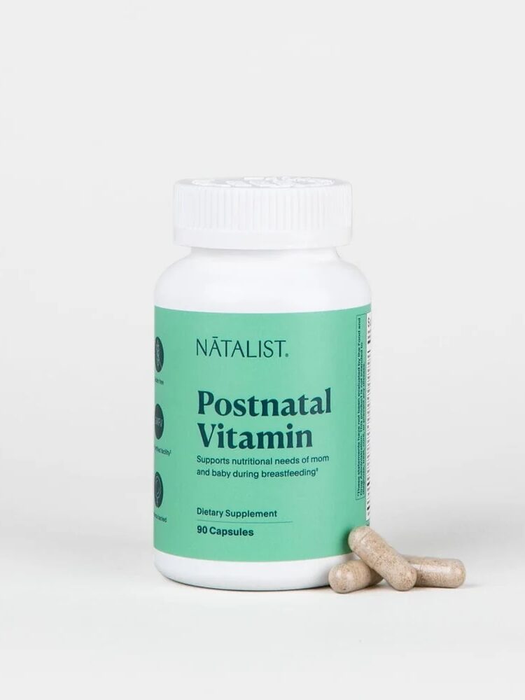 A bottle of Natalist Postnatal Vitamin capsules with a green label. Three capsules lie beside it.