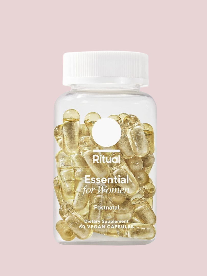 Clear bottle of Ritual Essential for Women Postnatal dietary supplements with 60 vegan capsules inside, against a pink background.