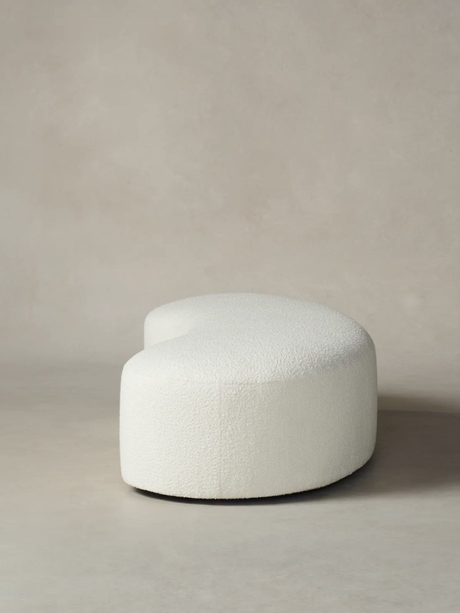 White, crescent-shaped ottoman against a plain gray background.