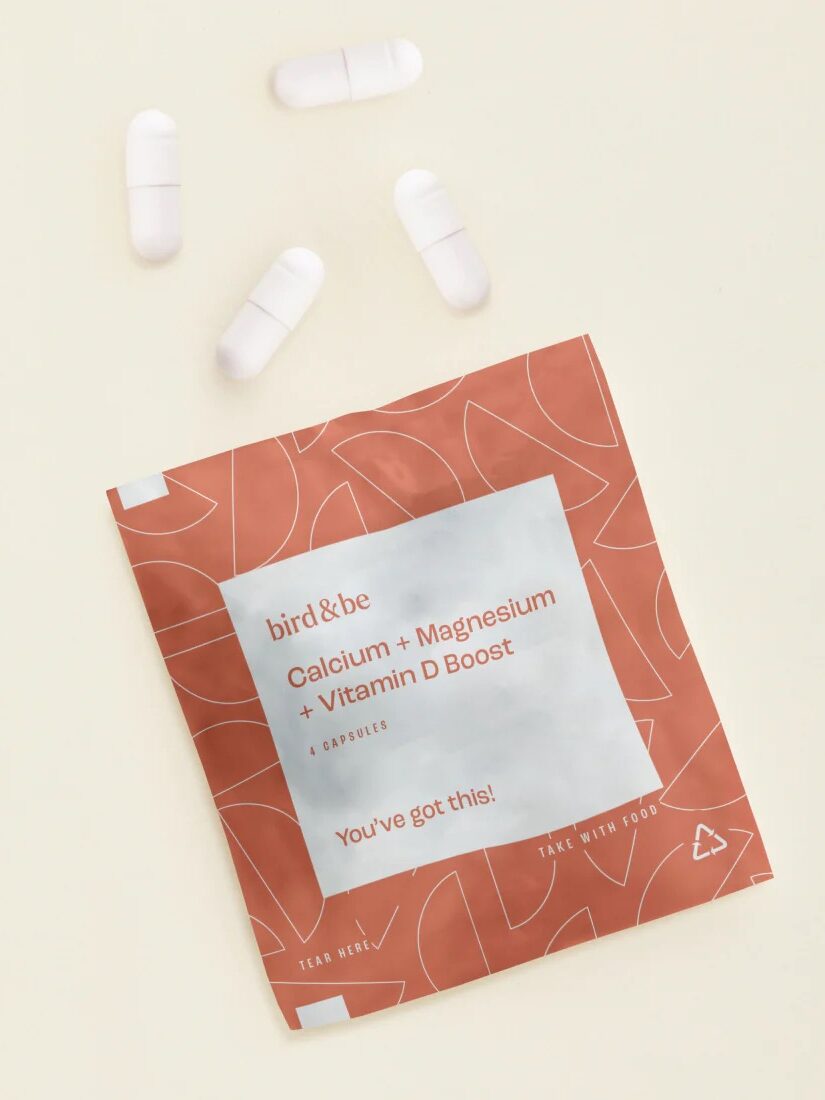A packet labeled "Calcium + Magnesium + Vitamin D Boost" lies flat with six white capsules scattered around it.