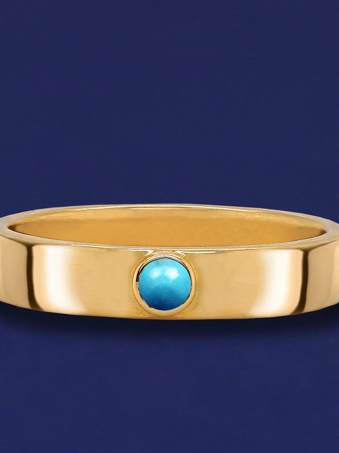 Gold ring with a turquoise stone set in the center against a blue background.