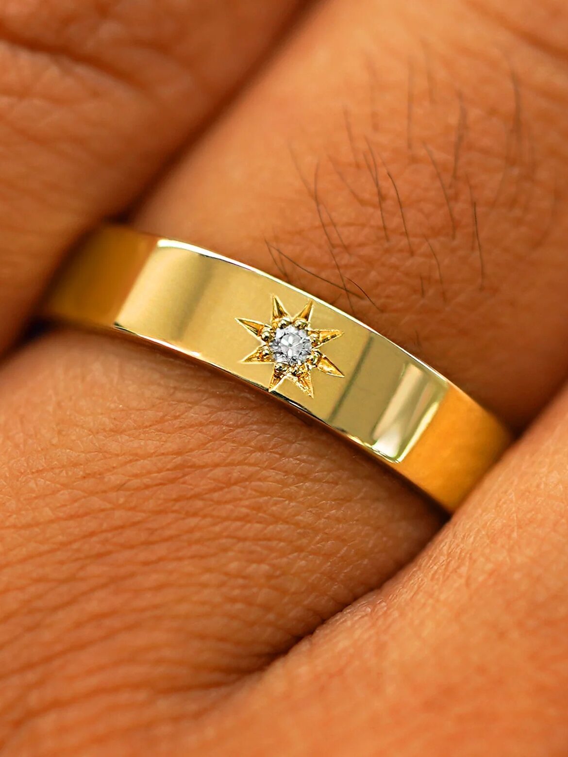 Gold ring with a small diamond in a star-shaped setting on a person's finger.