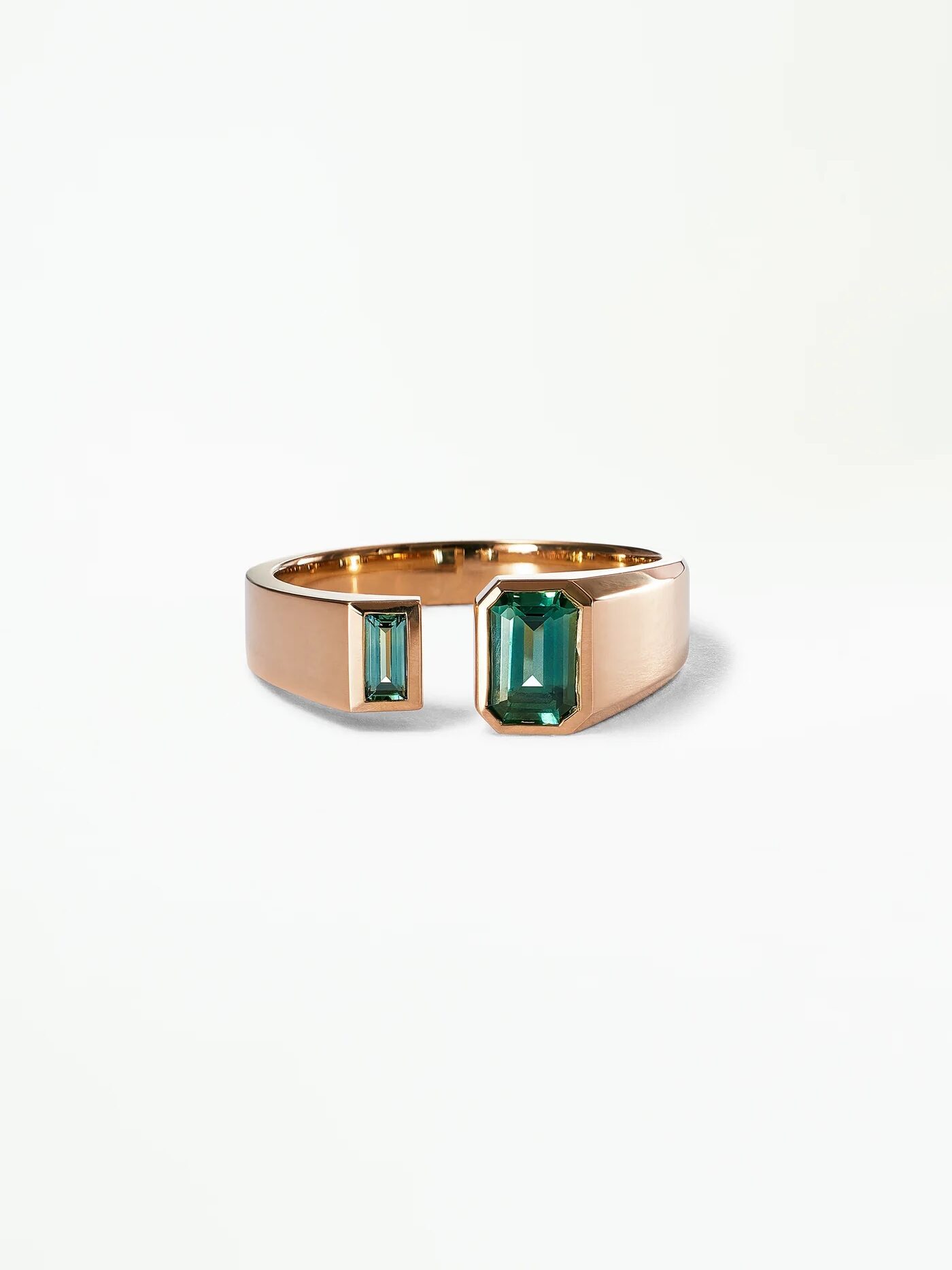 A gold open ring featuring two square-cut green gemstones against a plain white background.
