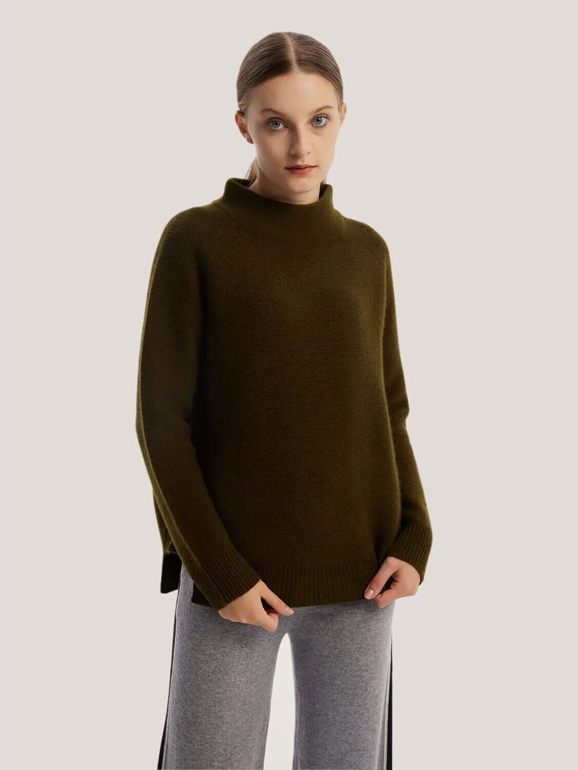 Person wearing a dark green turtleneck sweater and gray pants, standing against a plain background.