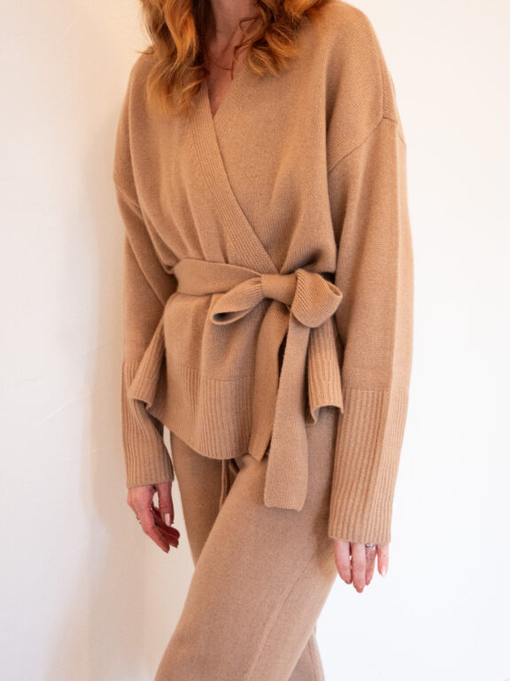 Person wearing a tan, belted knit sweater and matching pants, posed against a plain white background.