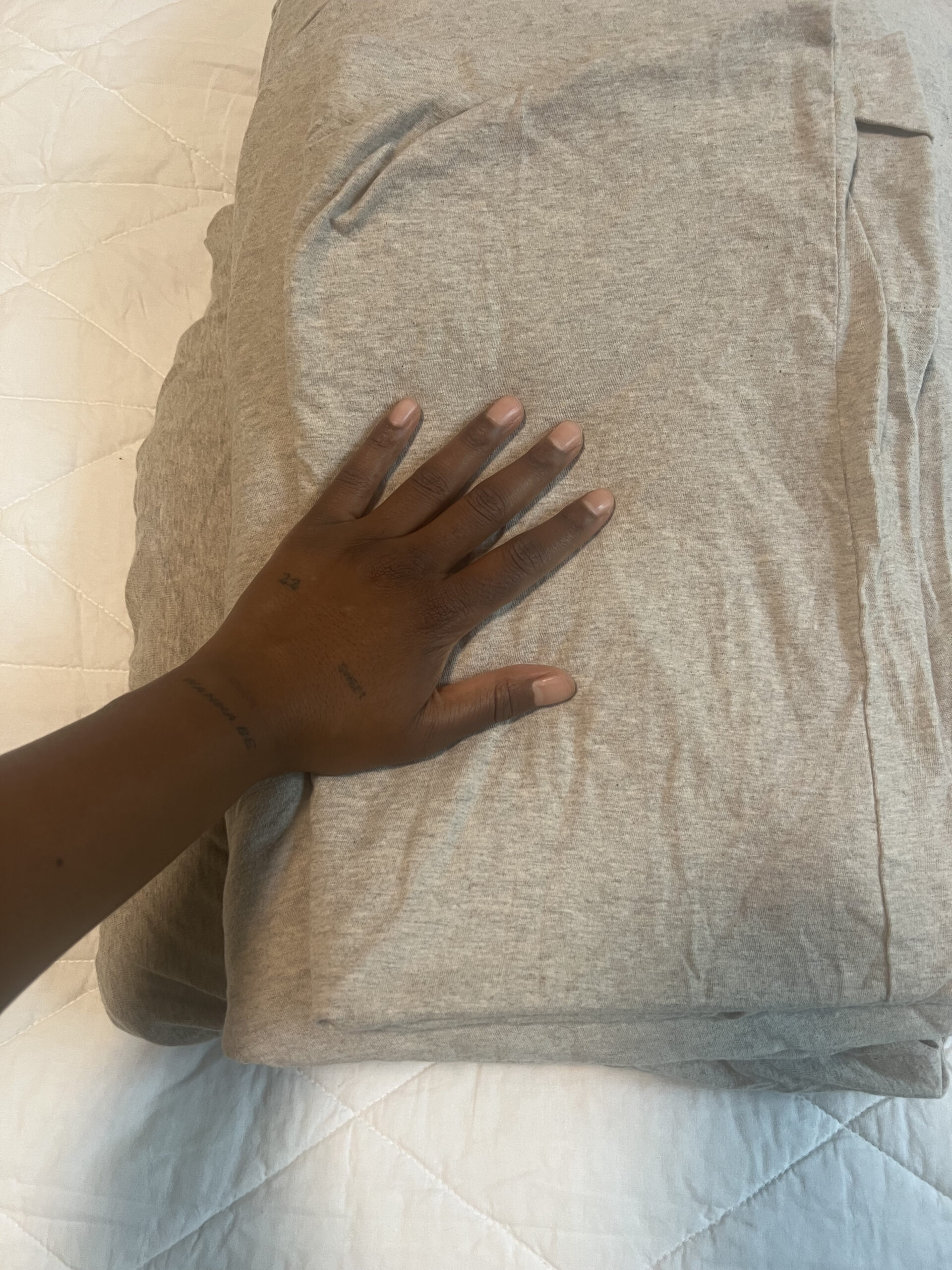A hand placed on top of a folded gray sheet on a white quilted surface.