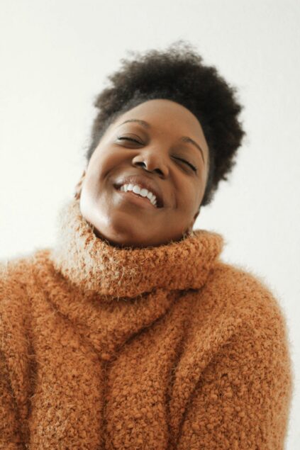 Person in a fuzzy brown sweater, smiling with closed eyes against a plain background.