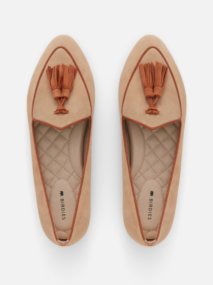 Tan woman's flat shoes with tassels on top, placed side by side on a white background. Quilted insoles are visible.