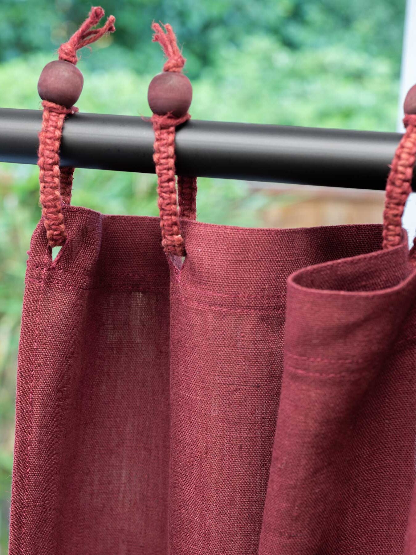 Close-up of red curtains hanging from a black rod with wooden beads, set against a blurred outdoor background.