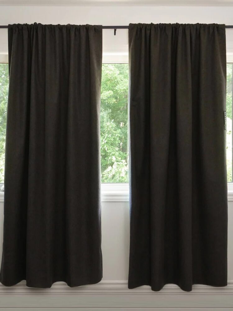 Two dark curtains hang on a rod above a window, partially covering a view of green trees outside.