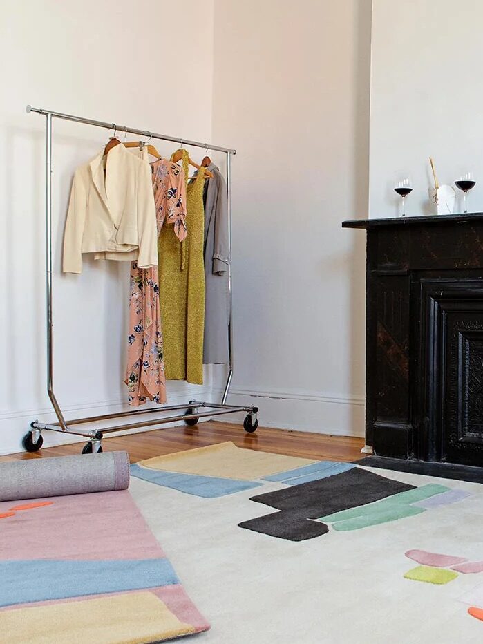 Room with a colorful abstract rug, black fireplace, clothing rack with garments, and cardboard boxes.