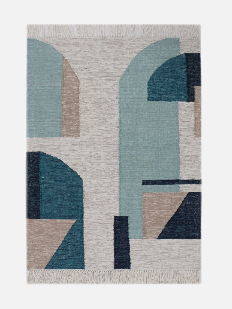 Rectangular rug with abstract geometric patterns in shades of blue, teal, beige, and dark blue, featuring fringed edges.