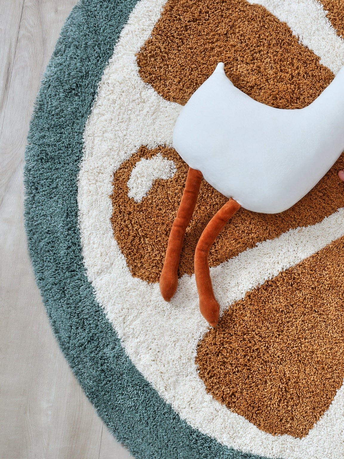 A baby lying on an orange and white circular rug, with a white and orange plush bird toy nearby.