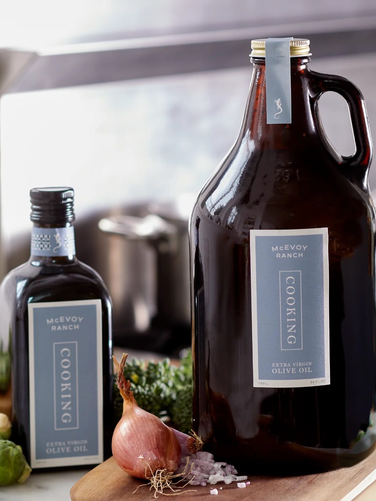 Two bottles of McEvoy Ranch cooking olive oil on a kitchen counter, surrounded by vegetables.