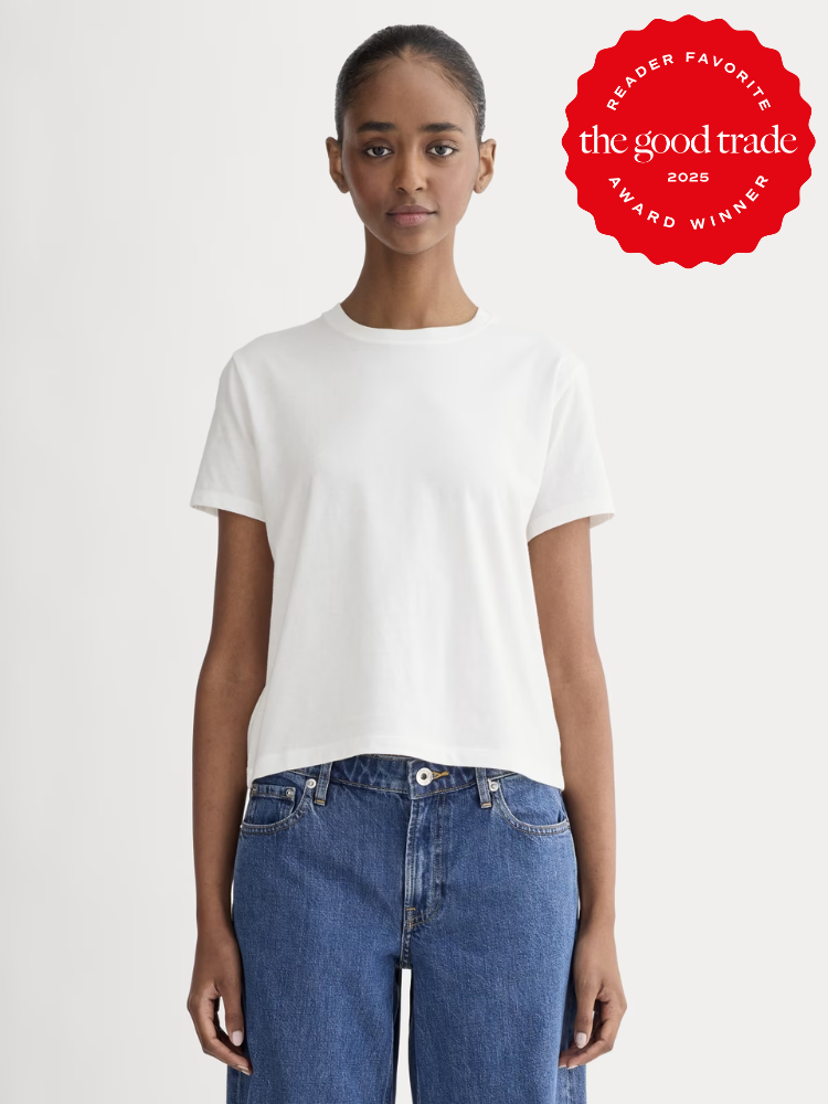 A person stands facing forward wearing a plain white t-shirt and blue jeans. A red award badge in the upper right corner reads "The Good Trade Reader Favorite Award Winner 2025.