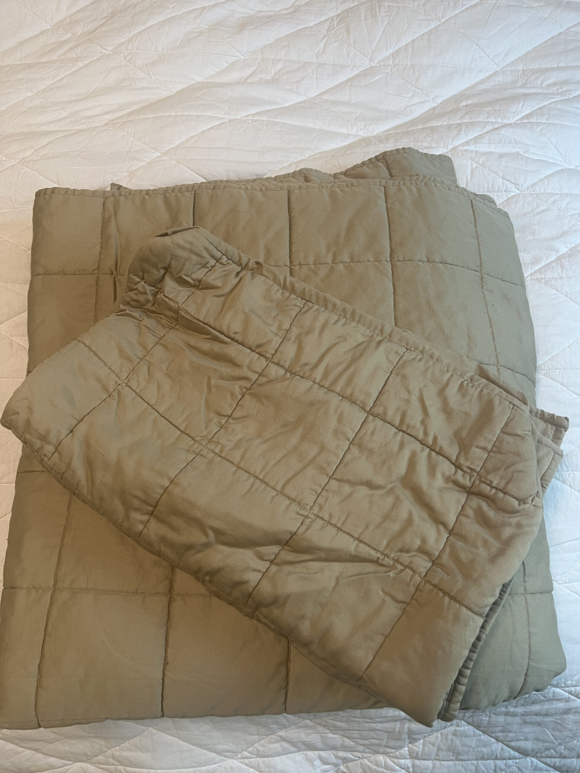 A folded green quilt with a grid pattern lies on a white bedspread.