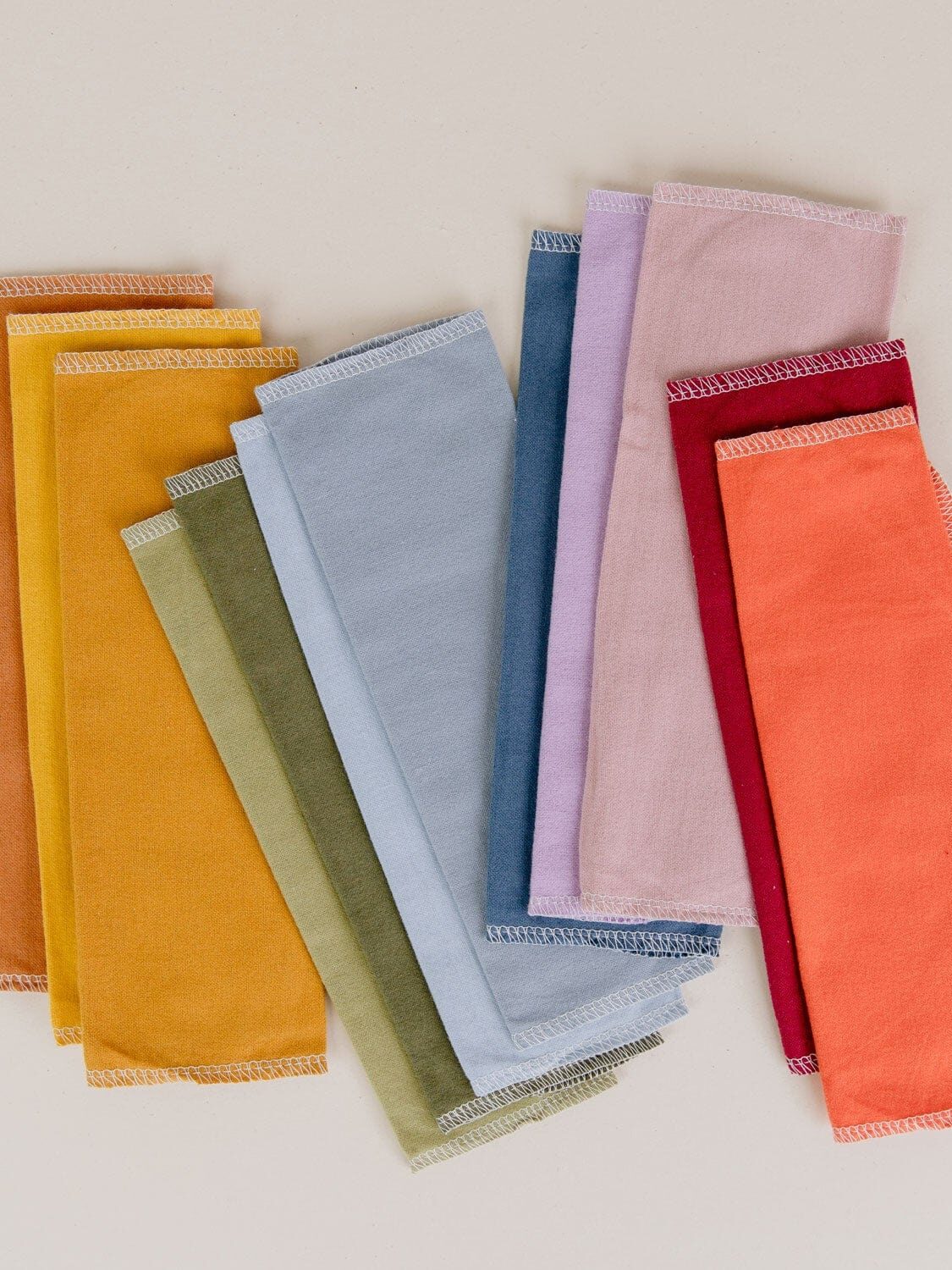 A collection of neatly folded cloth napkins in various colors, including yellow, green, blue, pink, red, and orange, arranged on a neutral background.
