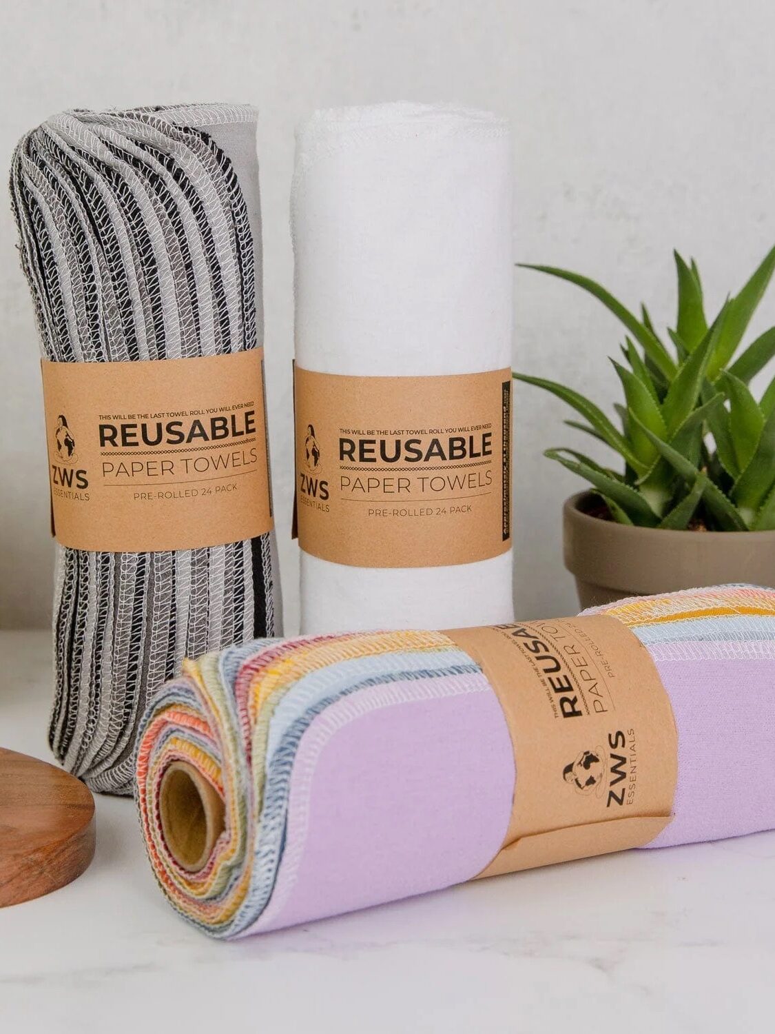 Three rolls of reusable paper towels in different colors on a countertop with potted succulents and sliced oranges nearby.
