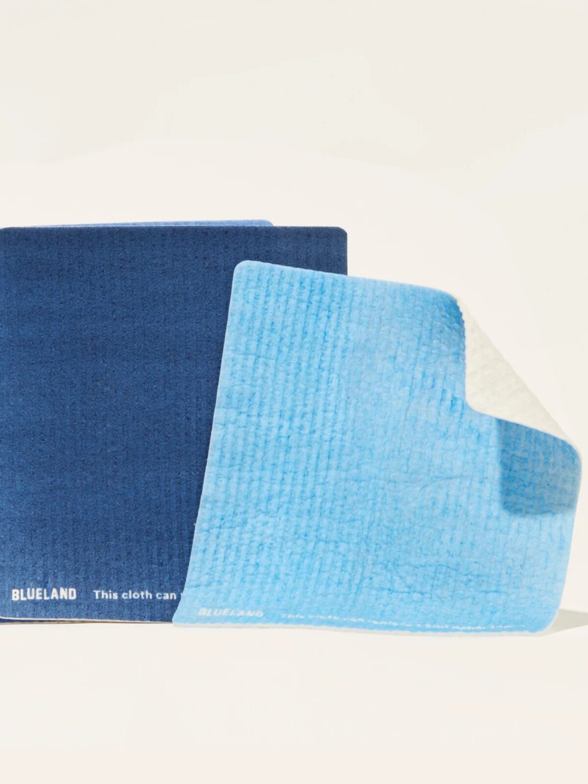 Three blue cleaning cloths, two stacked and one partially folded, on a light background.