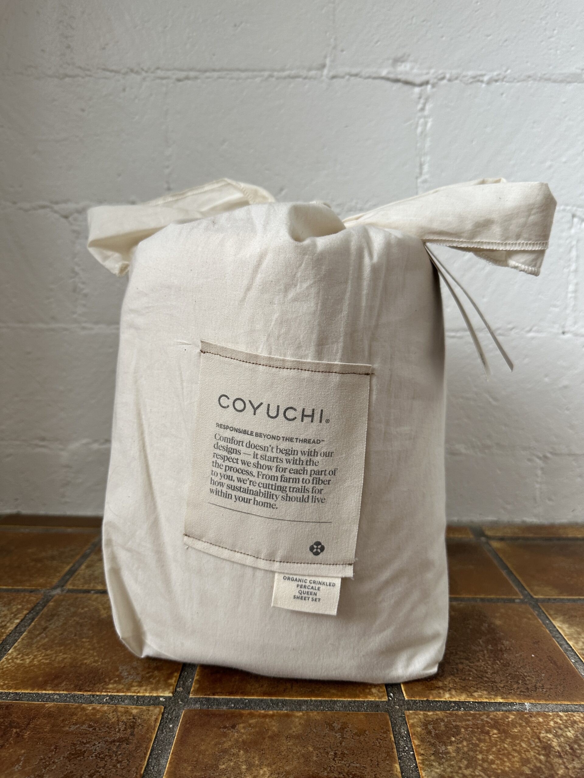 A fabric bag on a tiled surface, featuring a patch with text and branding related to Coyuchi.