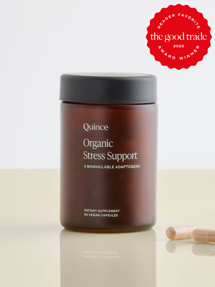 A brown jar labeled "Quince Organic Stress Support" sits on a beige surface with two capsules nearby; a red award badge appears in the top right corner.