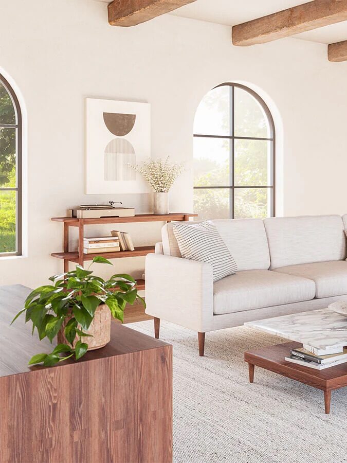 Modern living room with a beige sectional sofa, green armchair, wooden coffee table, and exposed ceiling beams. Large arched windows and a neutral color palette enhance the bright, airy space.