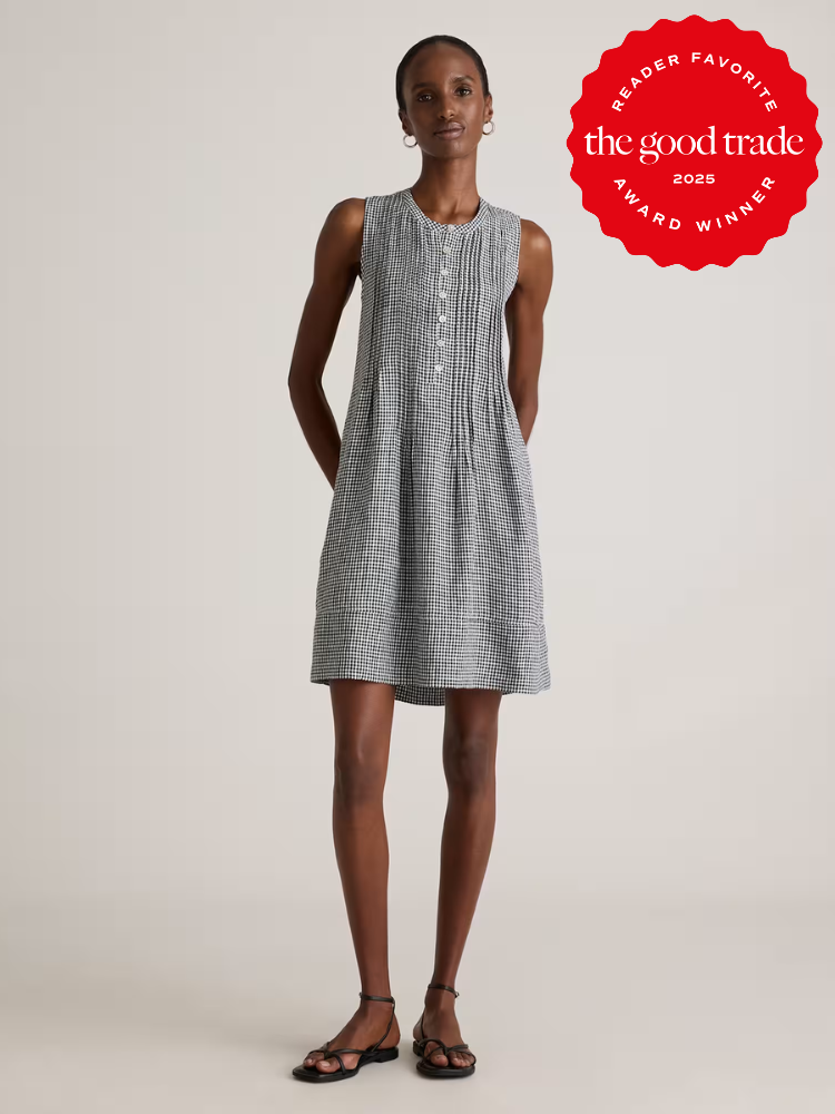 A woman wearing a sleeveless, button-front, black and white checkered dress stands with hands behind her back. A red "The Good Trade 2025 Award Winner" badge is in the top right corner.