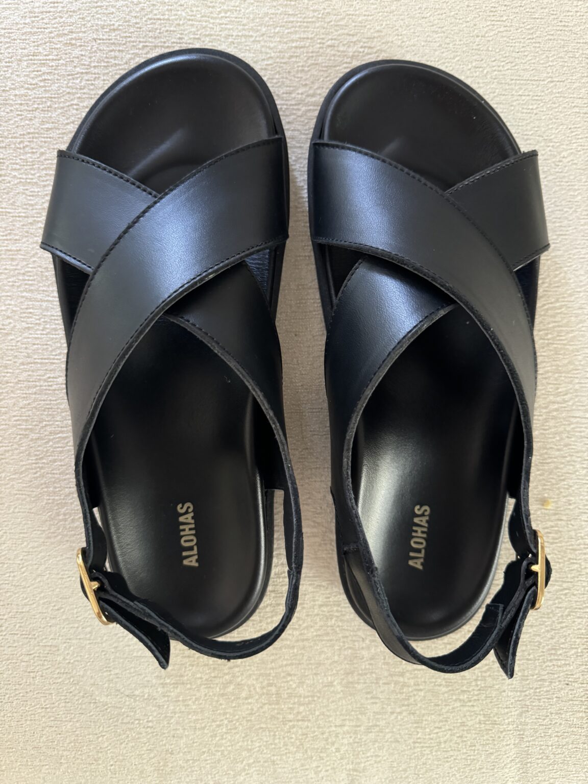 Black sandals with crisscross straps and a slingback buckle, viewed from above on a light surface.