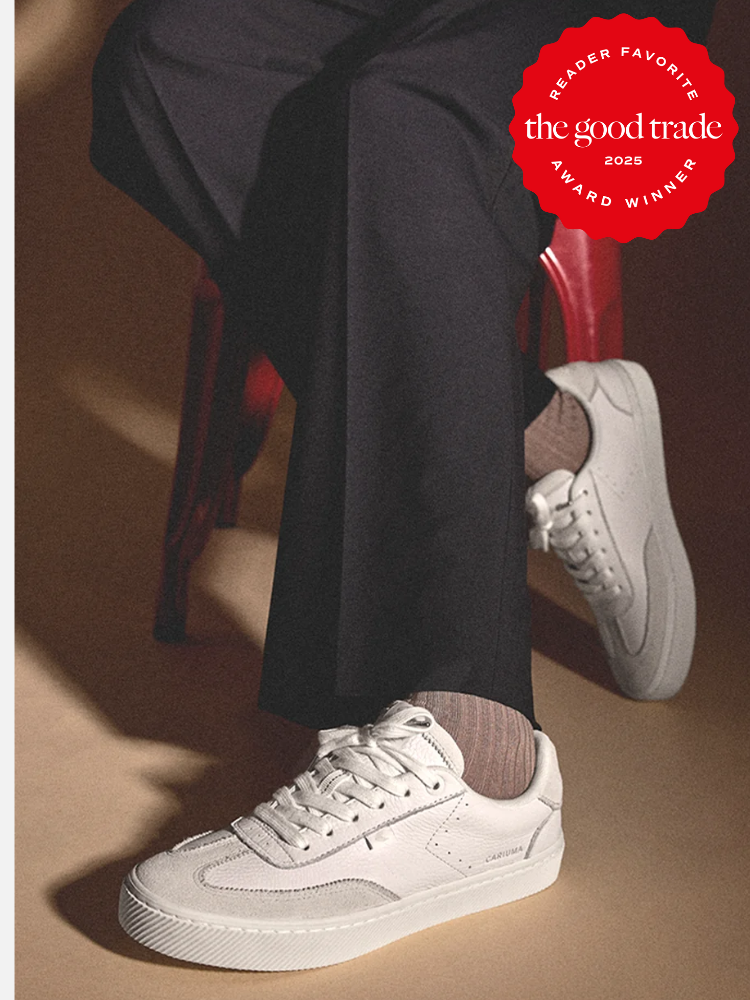 Person in dark pants seated on a red chair, wearing white sneakers and striped socks. A red badge in the top right corner reads "Reader Favorite The Good Trade 2025 Award Winner.