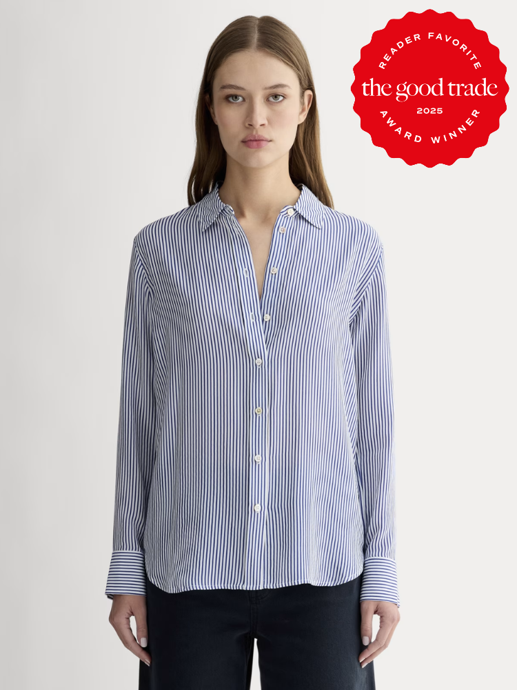 Woman wearing a blue and white striped button-up shirt stands facing forward; a red "The Good Trade Award Winner 2025" badge is displayed in the top right corner.