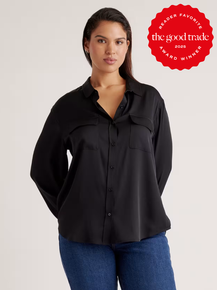 A woman wearing a black button-up shirt and blue jeans stands with her hands behind her back. A red "The Good Trade 2025 Award Winner" badge appears in the top right corner.