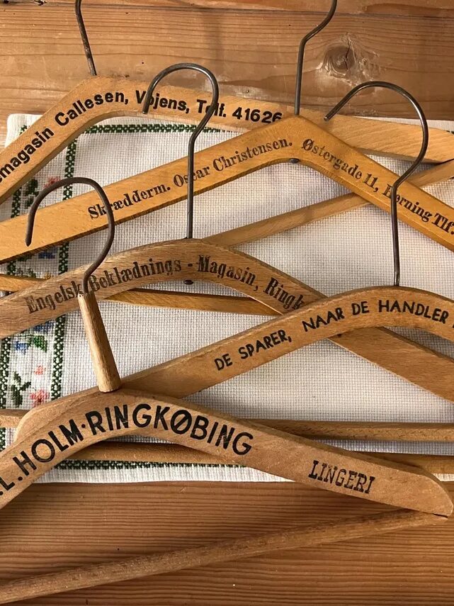 A collection of vintage wooden hangers with engraved text is arranged on a wooden table. A potted plant is partially visible in the corner.