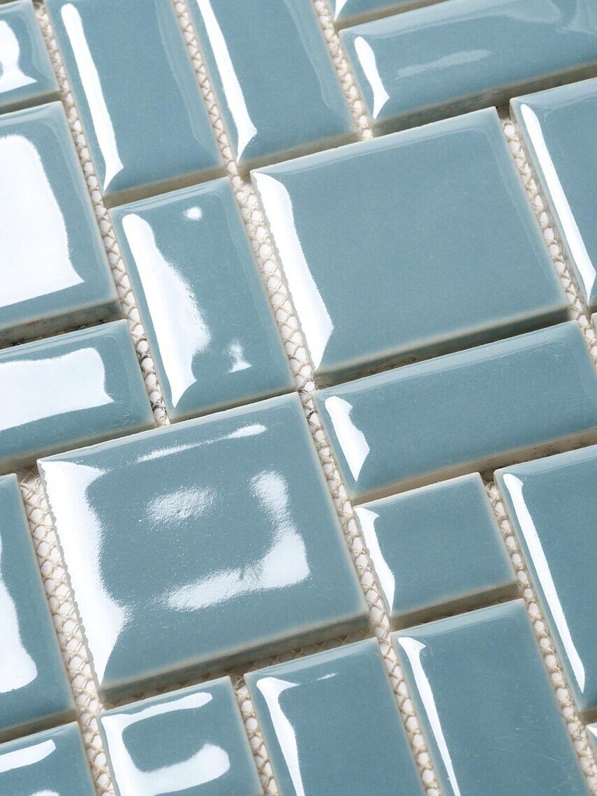 Close-up of glossy light blue square tiles with a slightly raised surface, arranged in a grid pattern.