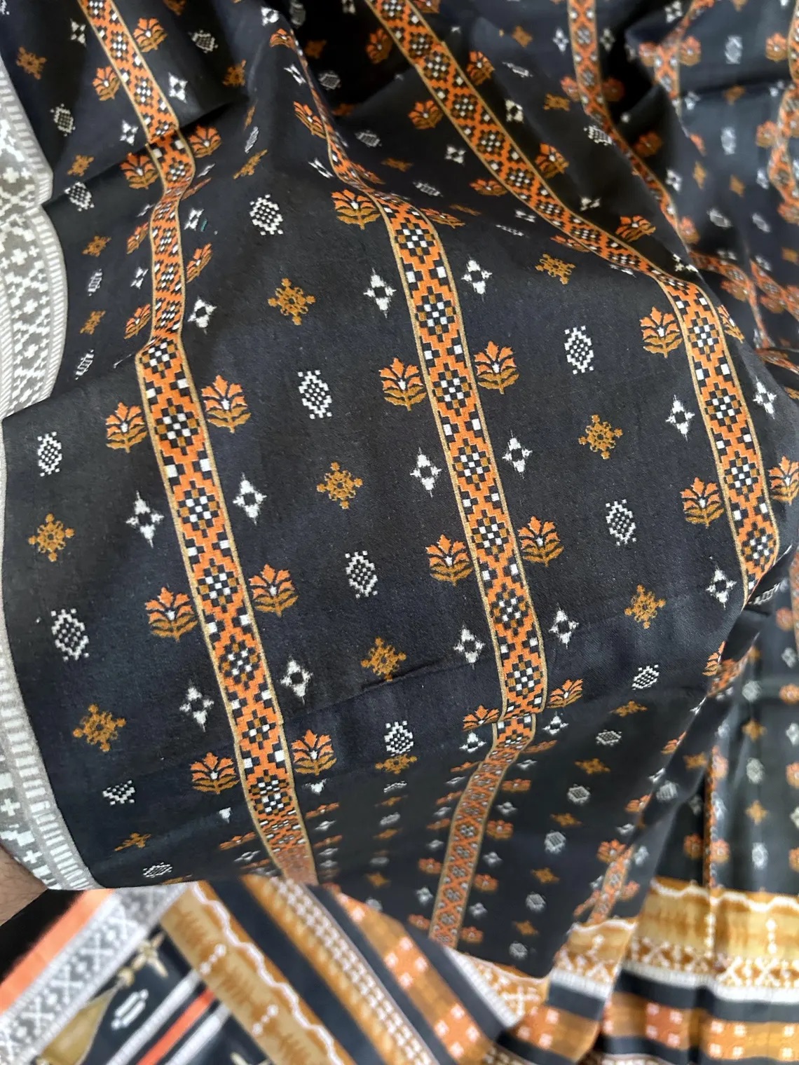 Close-up of a black fabric featuring orange and white geometric and floral patterns with stripes.