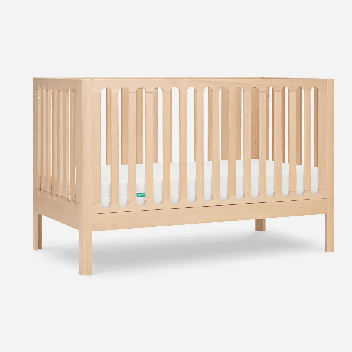 A natural wood baby crib with vertical slats on all sides and a white mattress inside, set against a plain white background.