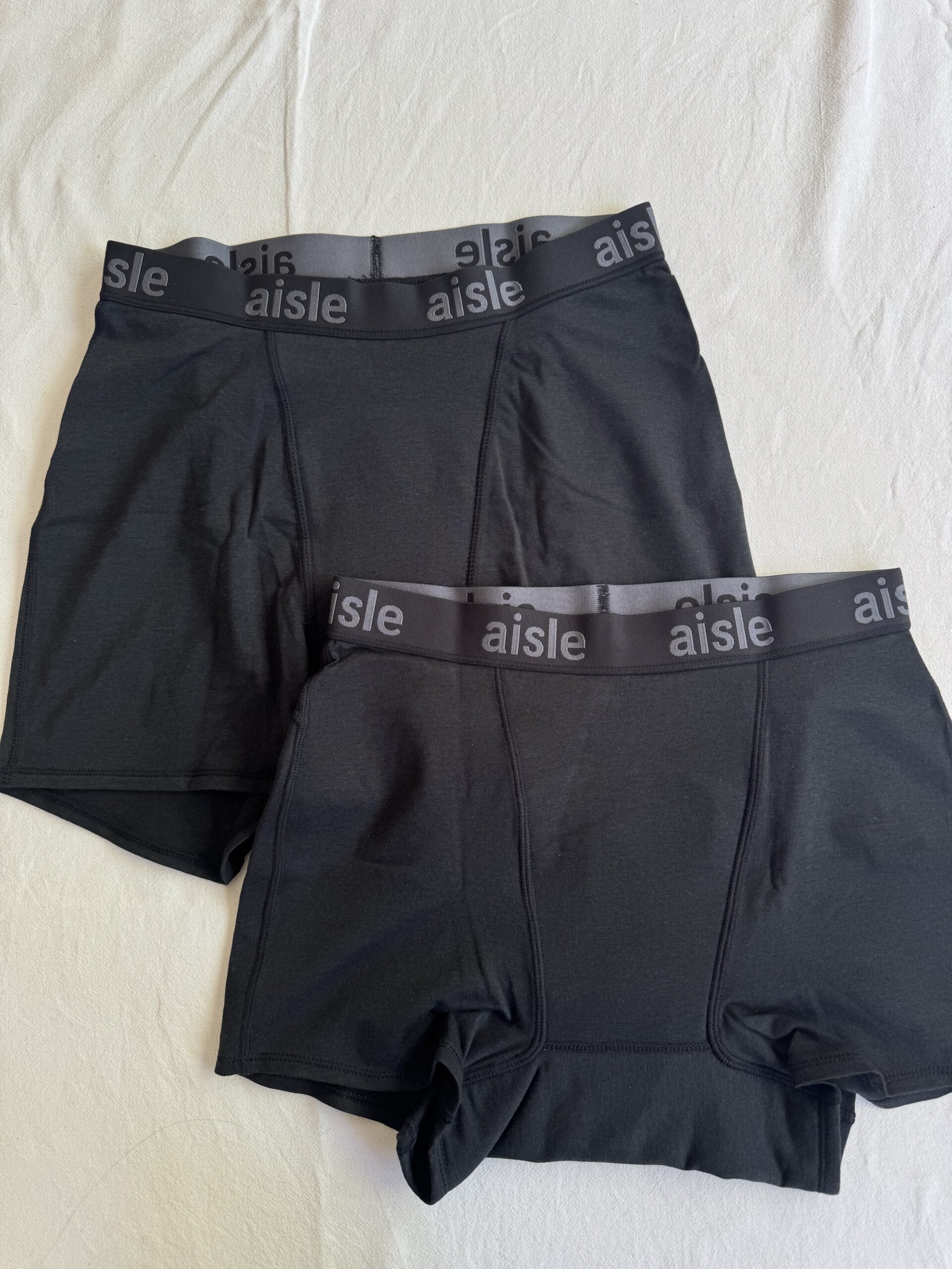 Two pairs of black boxer briefs with "aisle" printed on the waistband, laid flat on a white surface.