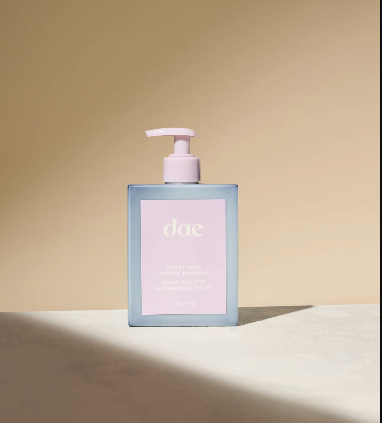 A bottle of "dae" violet hour purple shampoo with a pump dispenser, set against a neutral background in direct light.