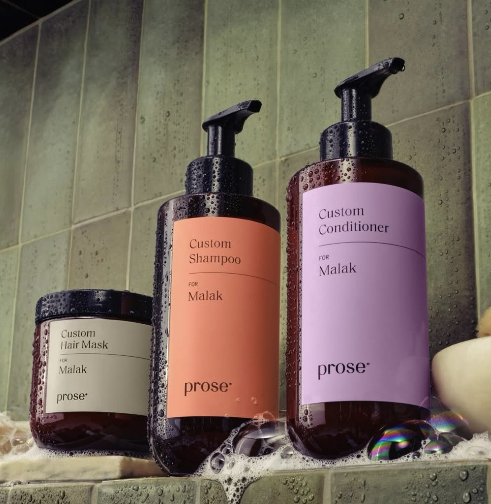 Three prose hair care products for "Malak" on a wet bathroom shelf: a custom hair mask, shampoo, and conditioner in labeled bottles.