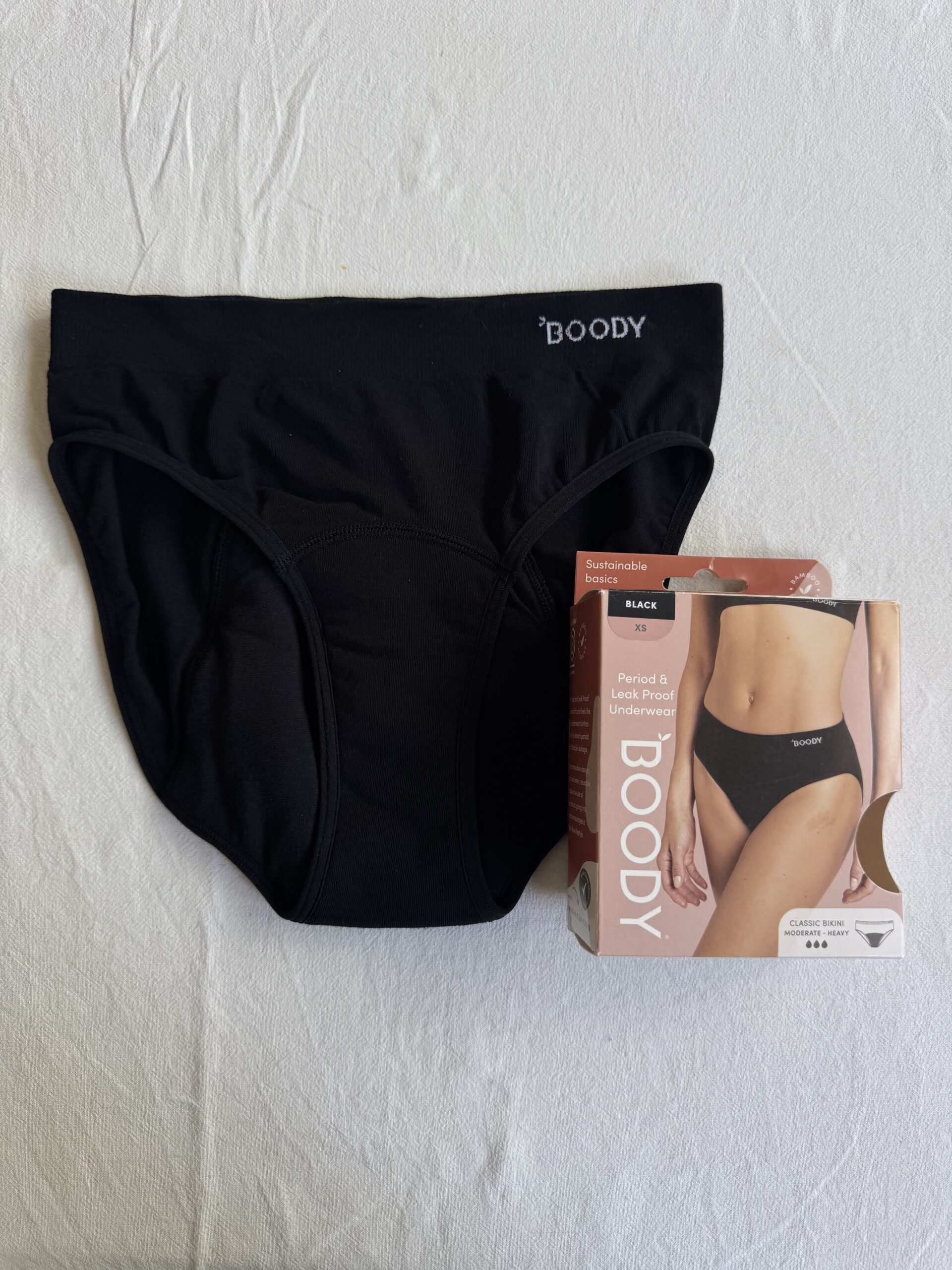 Black period and leak-proof underwear displayed alongside its packaging on a white surface.