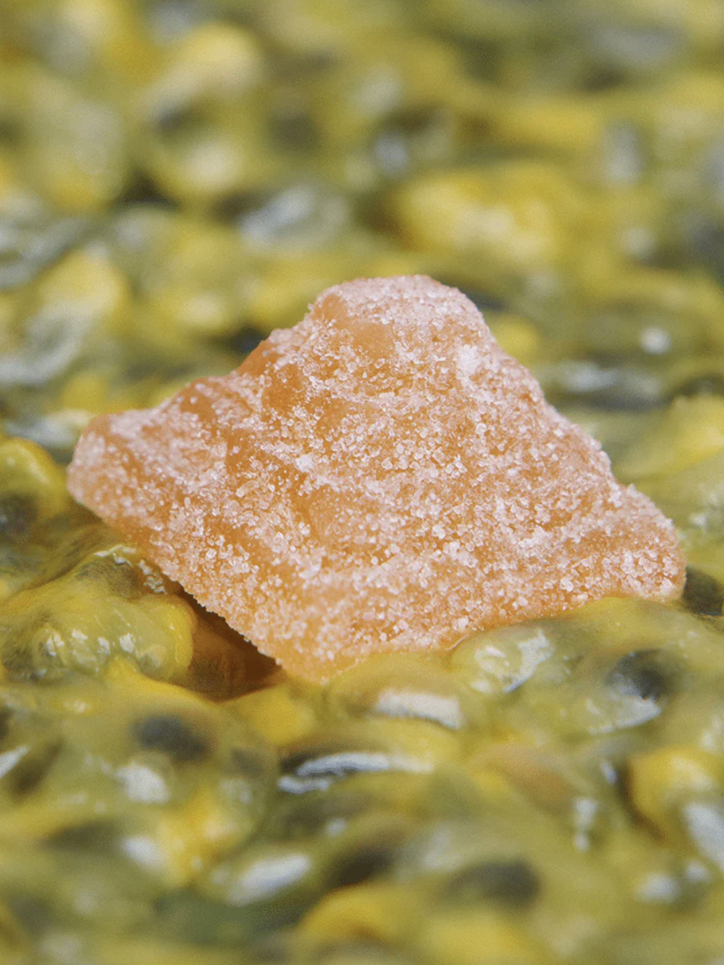 A sugar-coated orange gummy sits on a surface covered with passion fruit pulp and seeds.
