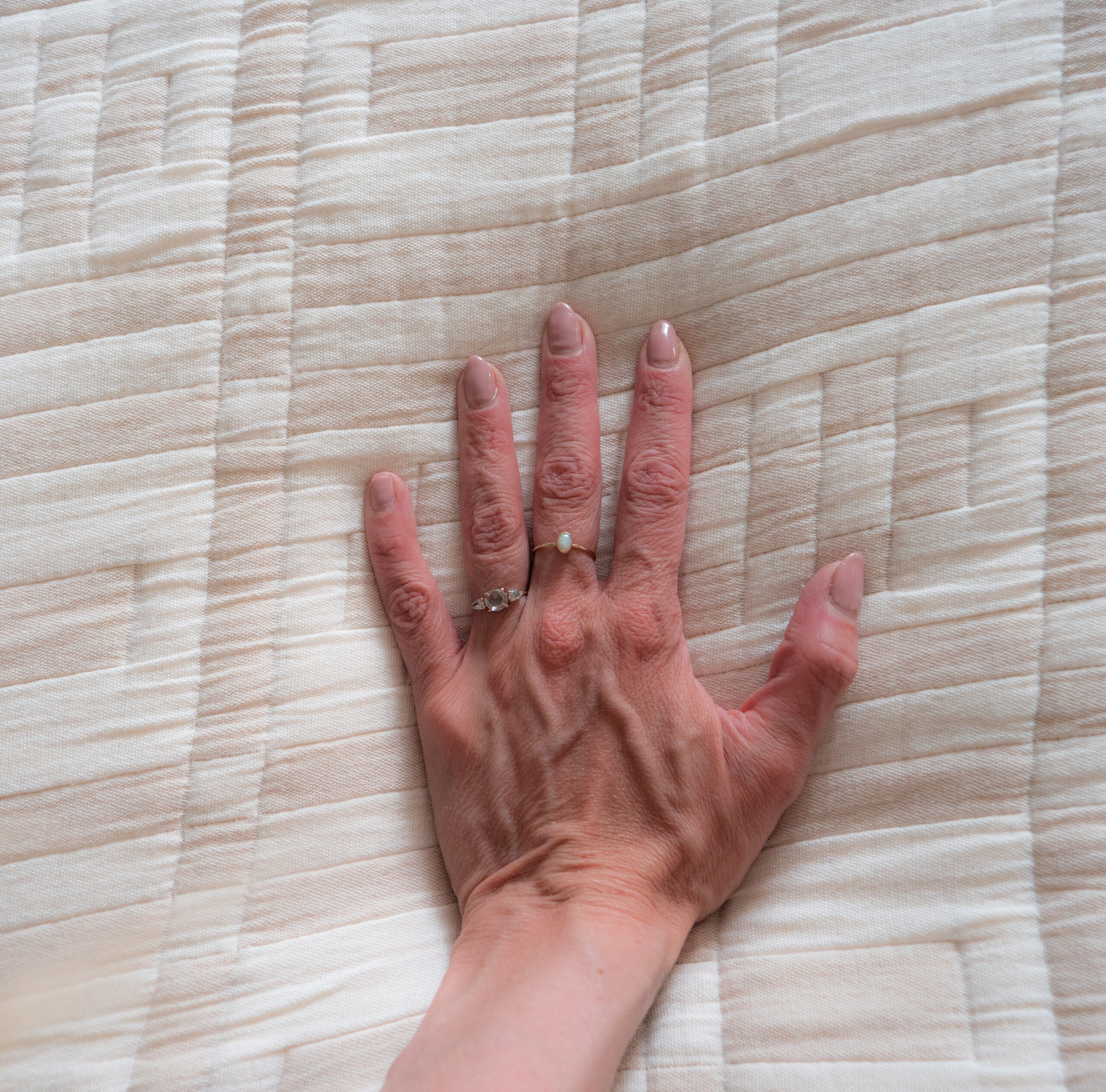 A hand with two rings rests on a textured, cream-colored surface with horizontal and vertical lines.