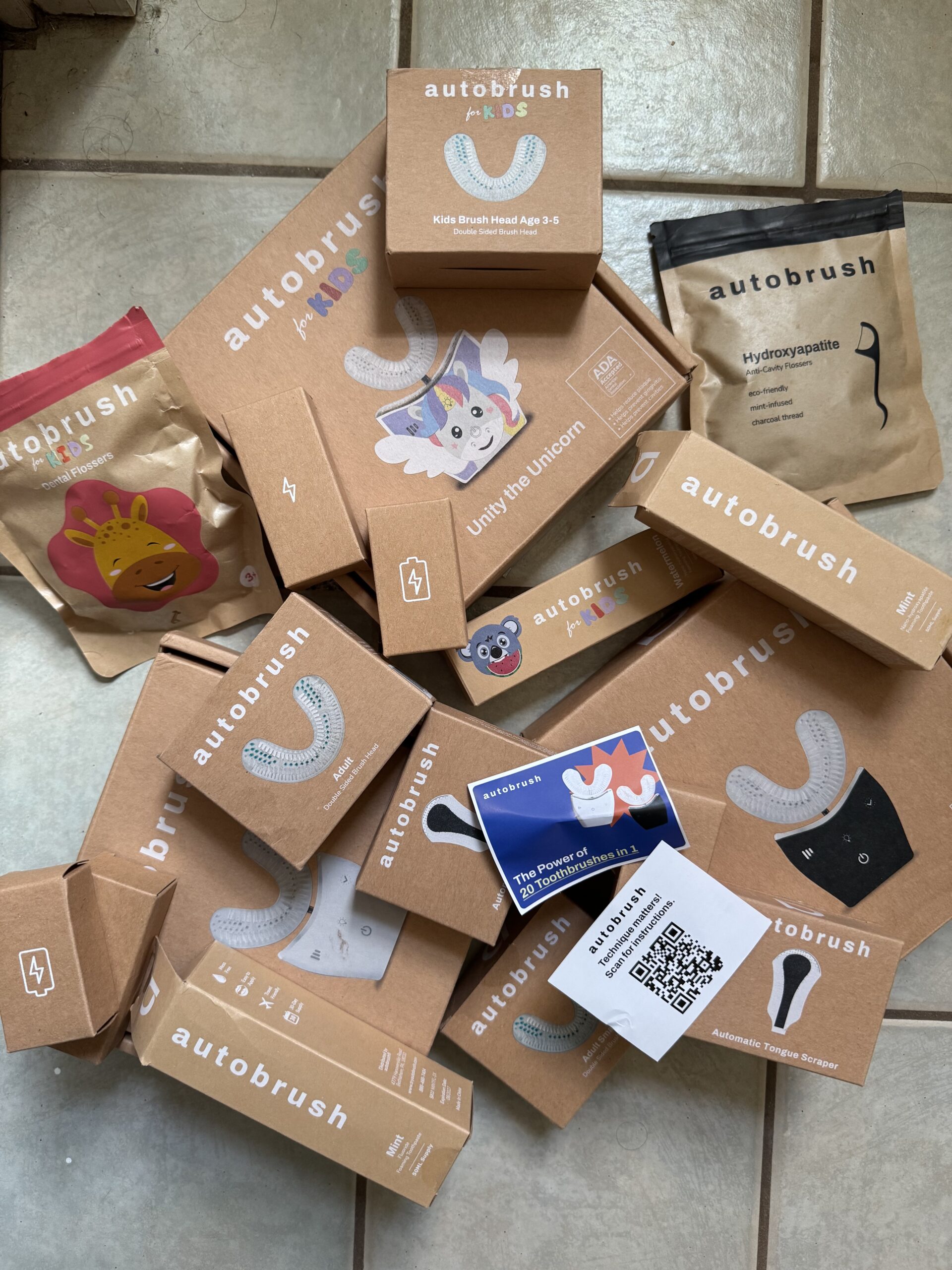 A collection of various Autobrush product boxes, including kids' models and accessories, scattered on a tiled floor.
