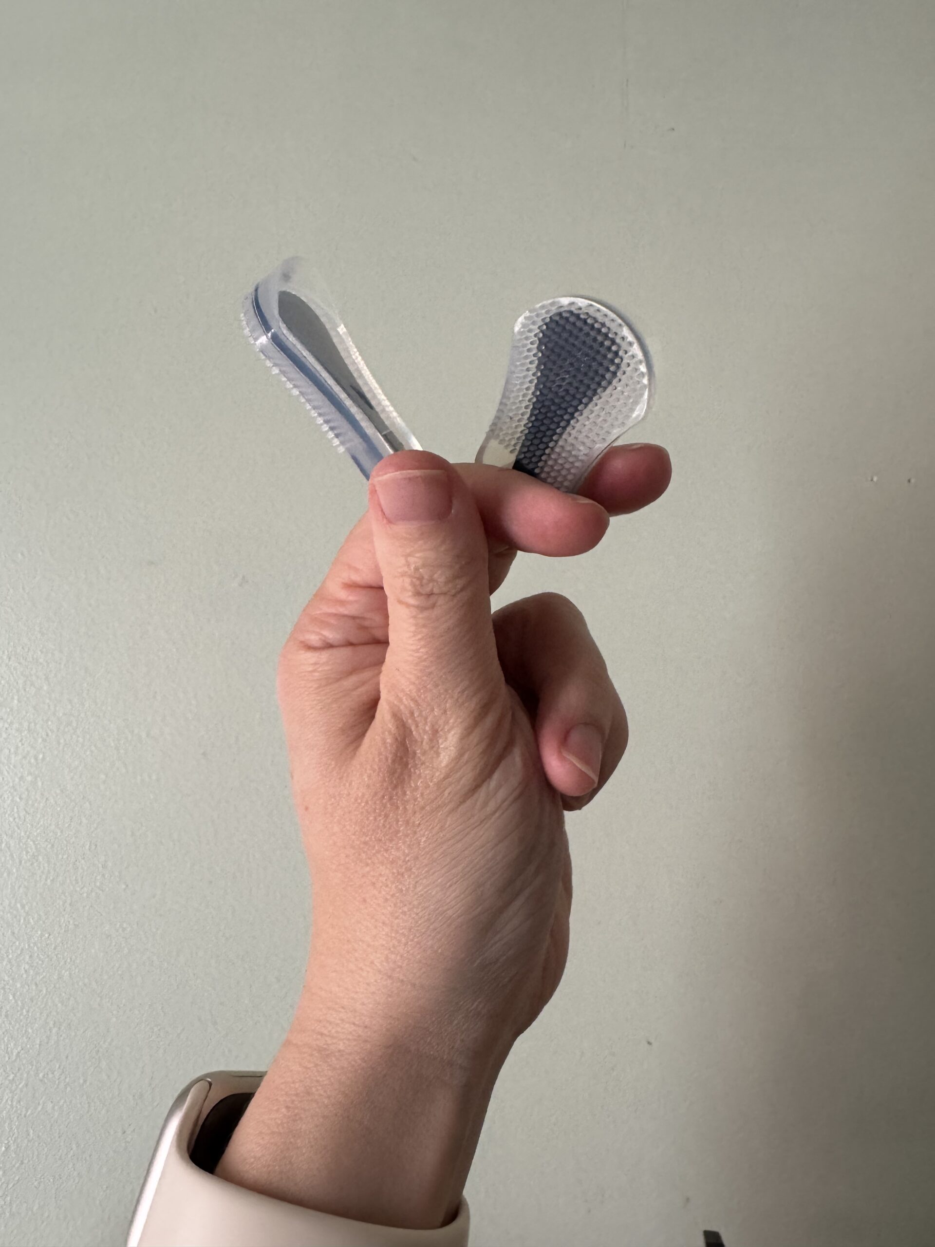 A hand holding a transparent dental aligner against a plain backdrop.
