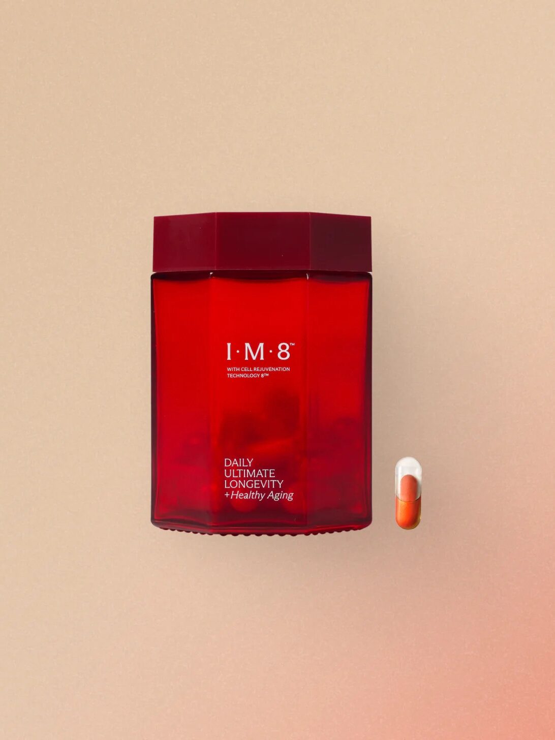 Red container labeled "I.M.8 Daily Ultimate Longevity + Healthy Aging" next to an orange and white capsule on a beige background.