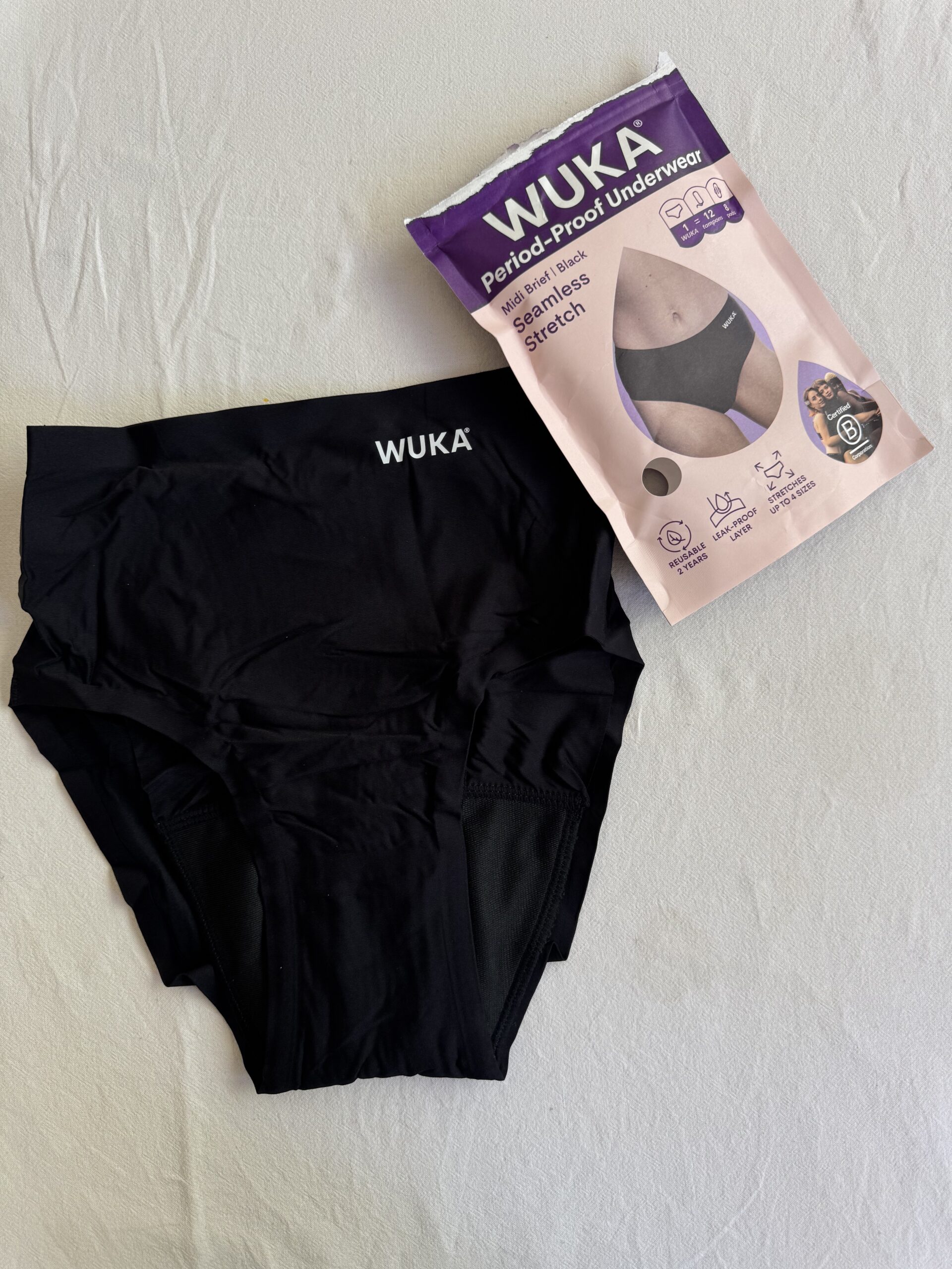 Black WUKA period-proof underwear next to packaging on a light surface. Packaging details features like seamless design and absorbency level.