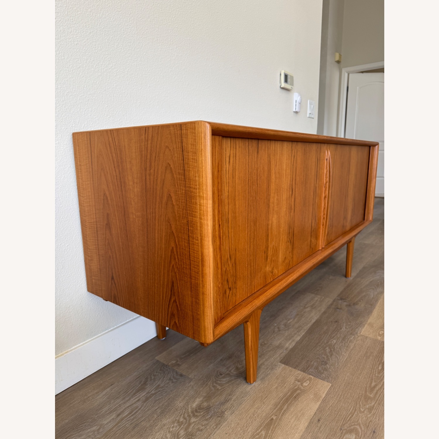 Mid-century modern wooden sideboard with clean lines and tapered legs, placed against a white wall on a wood floor.