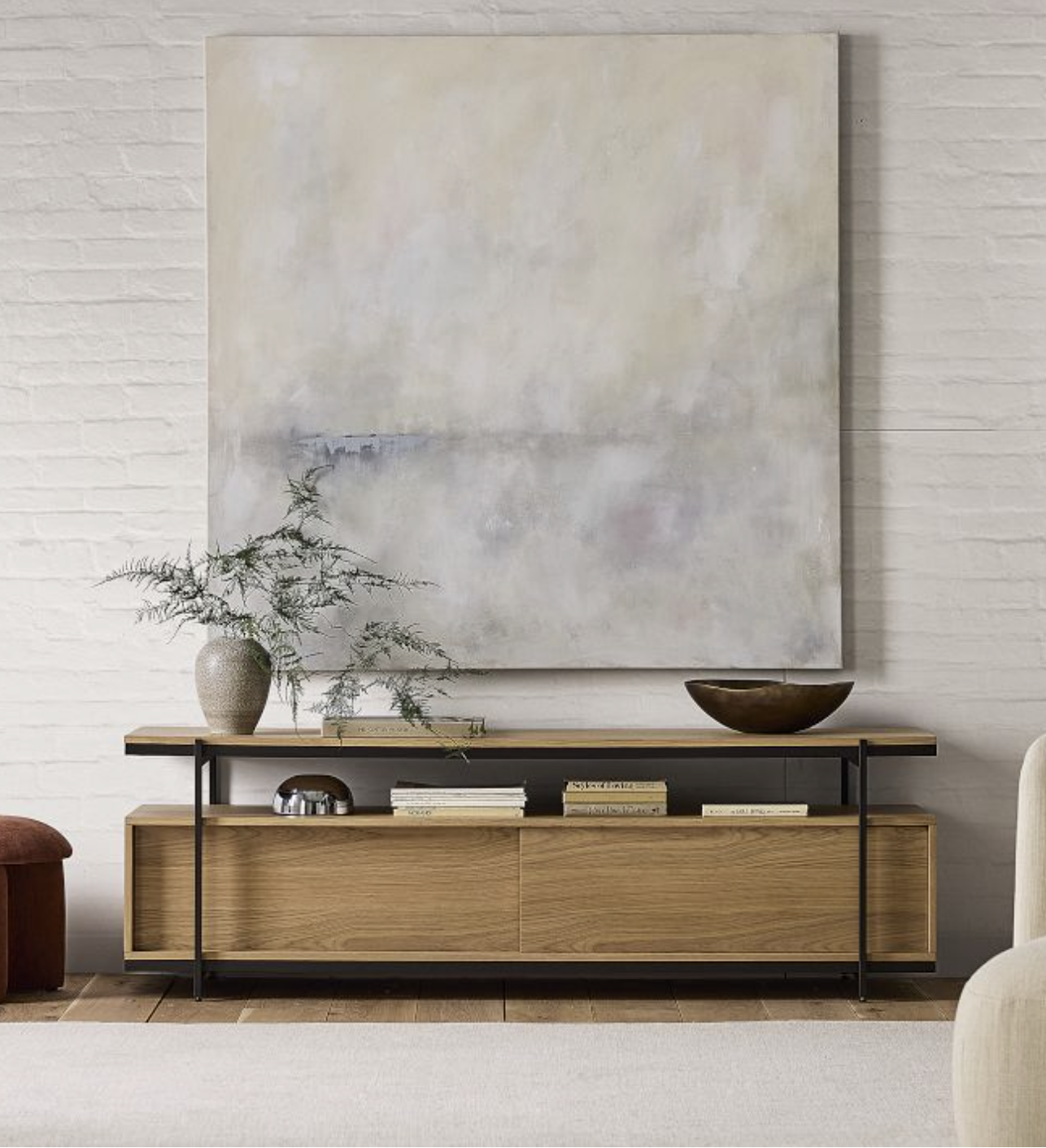 A minimalist living room scene with a wooden console table, decorative objects, books, and a large abstract painting on a white brick wall.