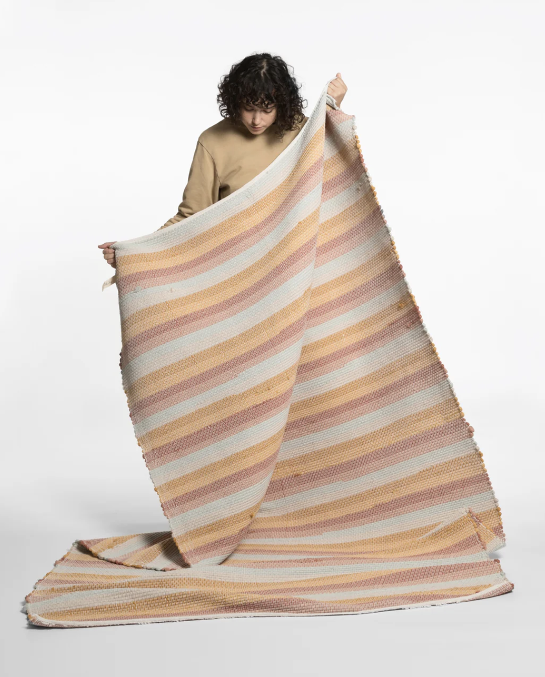 Person holding a large striped blanket with pink, orange, and white bands against a plain white background.