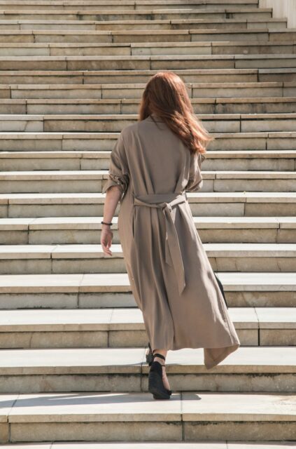 Person with long hair in a brown coat walking up wide stone steps.