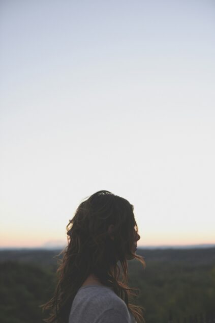 Silhouetted person with wavy hair stands against a clear sky at sunset.